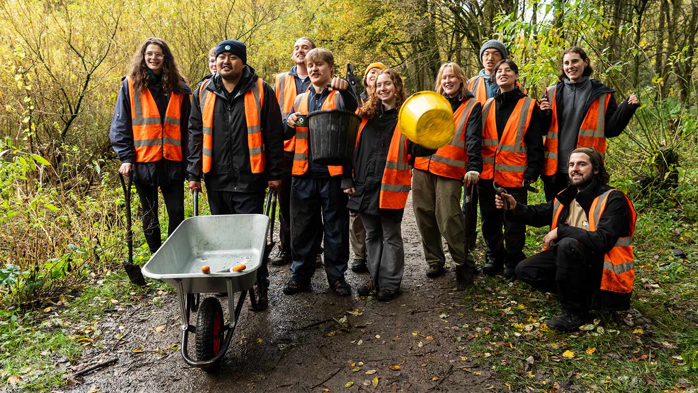 Greoup of people with wheelbarrow in woodland.