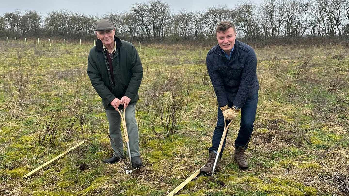 Two people posing with shovels in field.