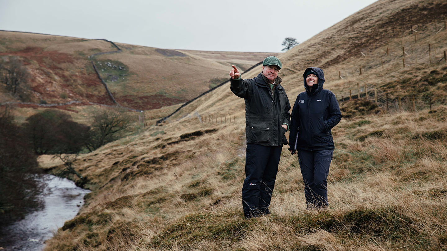 Two people talking beside stream in moorland.